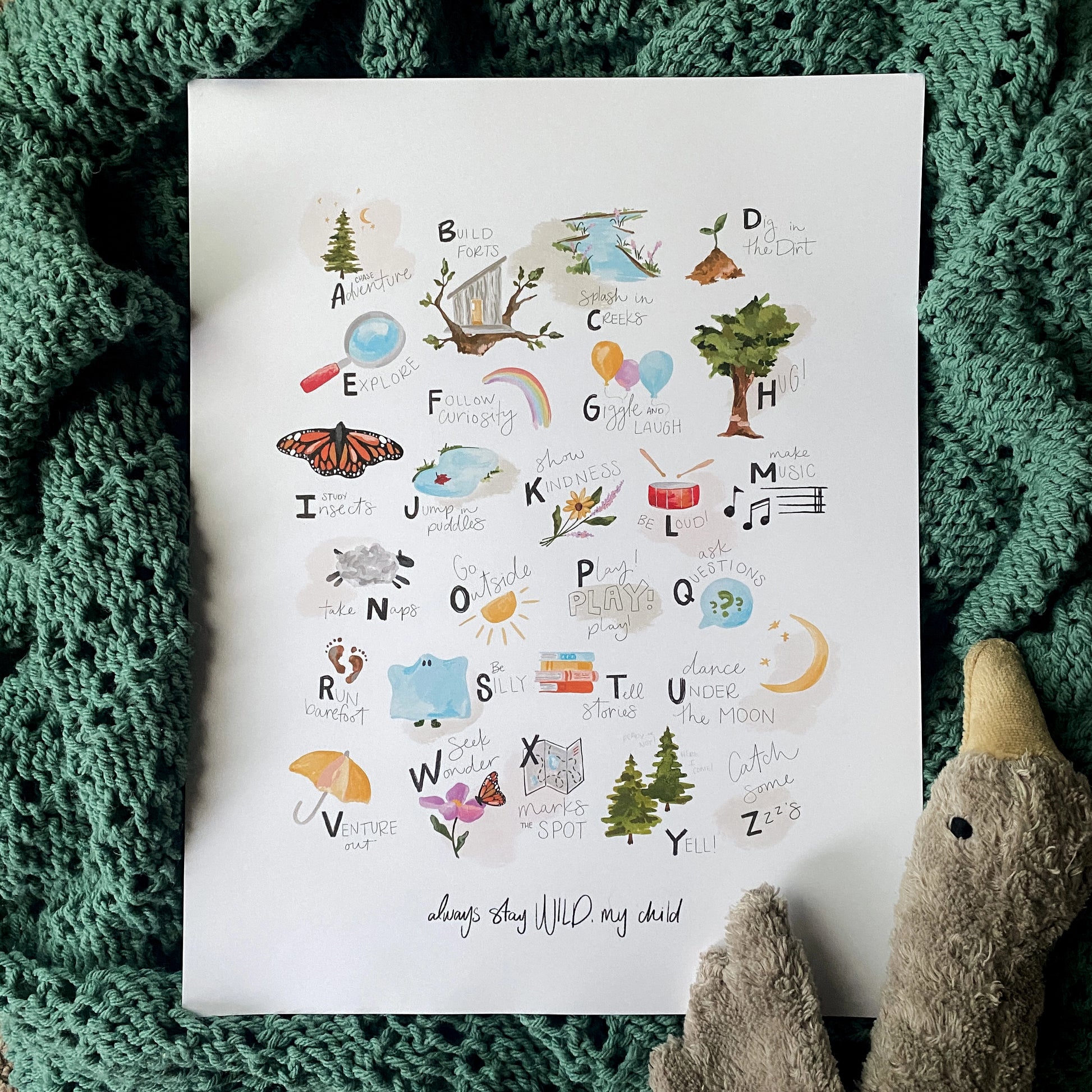 ABCs of Childhood alphabet art print by Stray Folk. laying on baby blanket with a stuffed goose